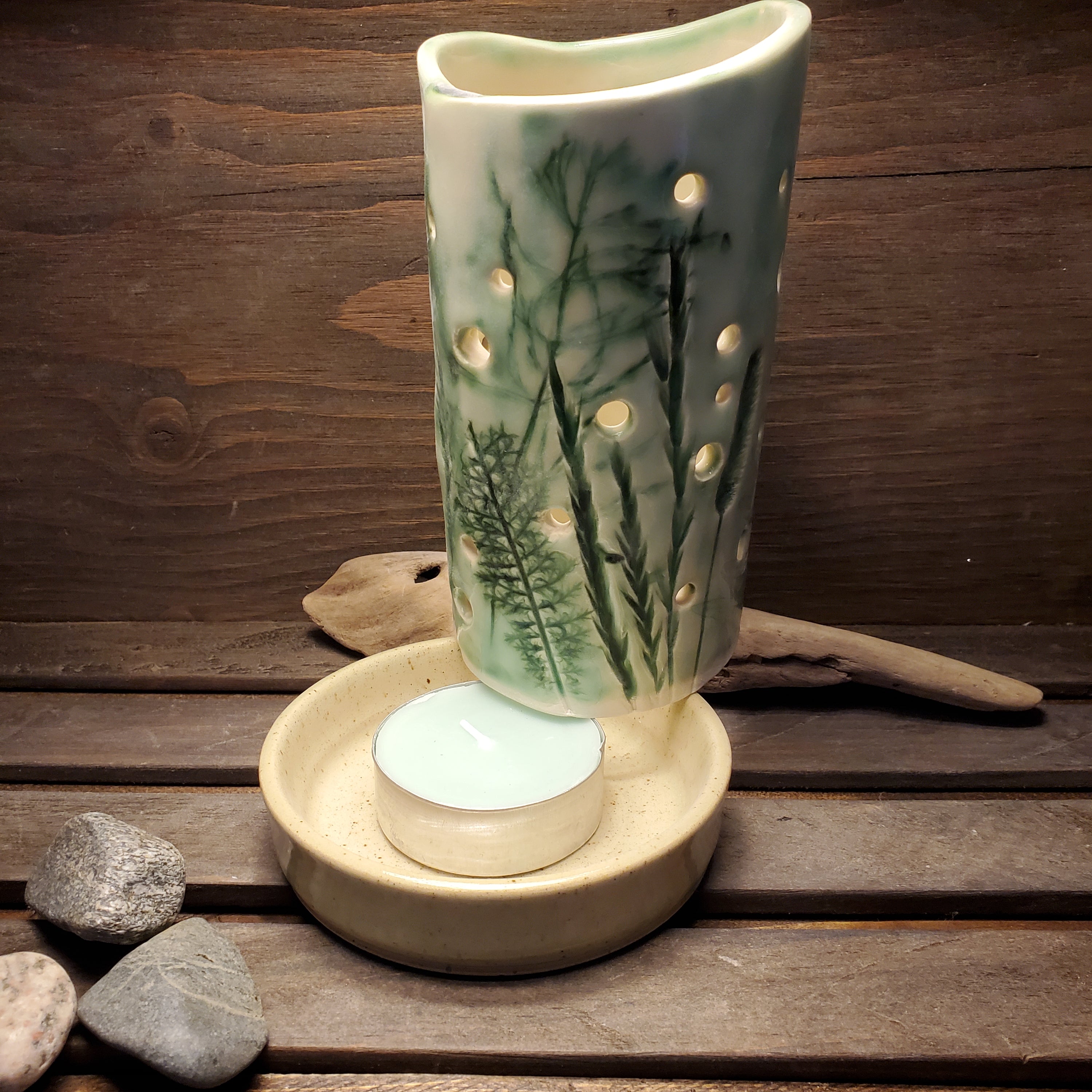 A green and white hand made pottery candle holder with a botanical design.
