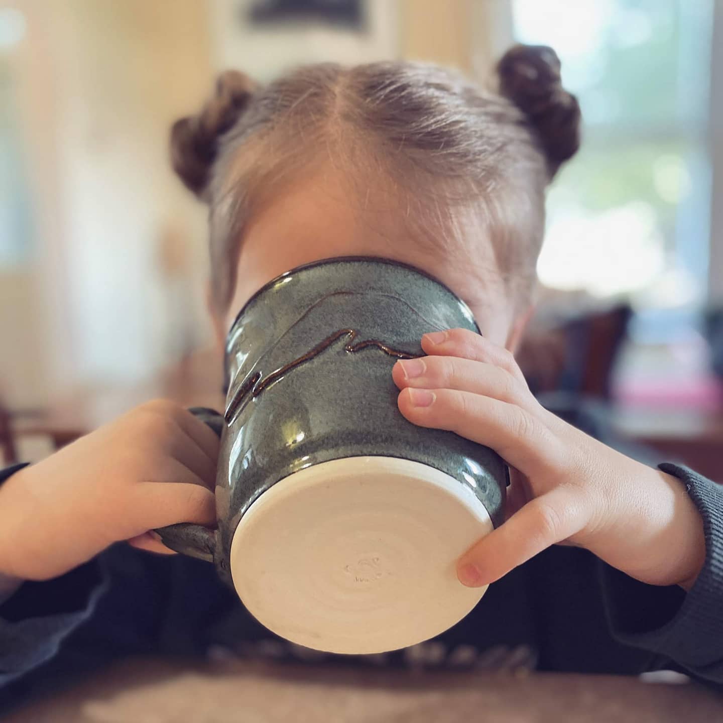 A young girl drinking out of a dark green, Green Cabin Pottery mug.