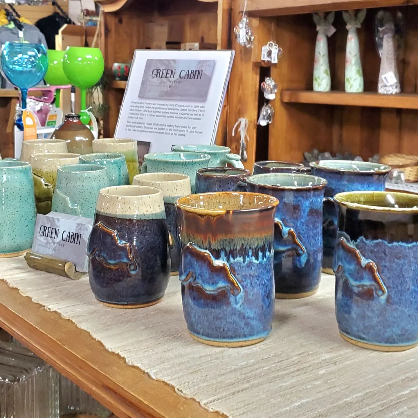Hand made pottery, pottery gifts, and ceramics displayed at a market in Wawa, Ontario. The selection of hand made pottery is assorted including: hand made coffee mugs and  hand made mugs. The pottery all features a Lake Superior design.