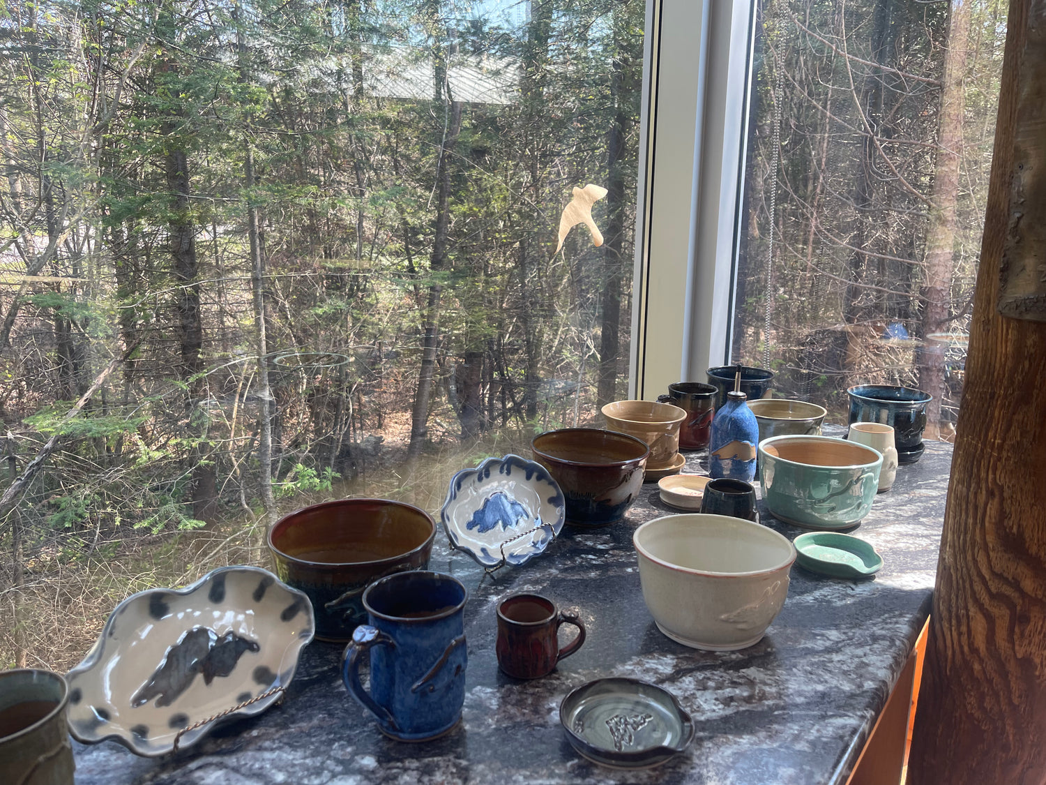 A selection of hand made pottery and ceramics made by Green Cabin Pottery displayed at the Agawa Visitor's Centre in Lake Superior Provincial Park. The assortment includes pottery gifts, hand made mugs, hand made bowls, hand made plates and other hand made pottery items - all of which feature a Lake Superior design on them.